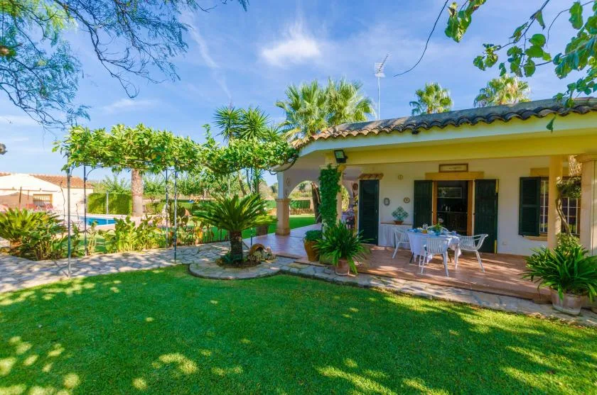 Un patio ajardinado junto a una casa, con asientos al aire libre y plantas frondosas.