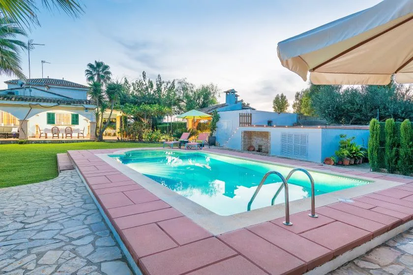 Una piscina al aire libre junto a un patio pavimentado y un jardín ajardinado.