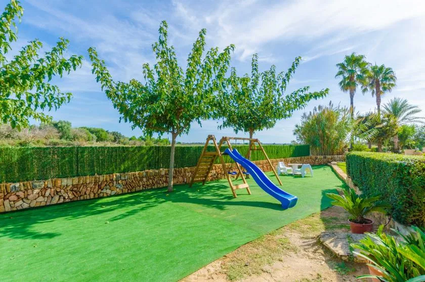 Zona de juegos en un jardín con un tobogán azul y césped artificial verde.