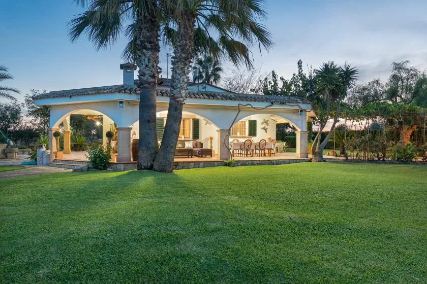 Una casa de una planta con un patio cubierto de arcos da a un amplio césped verde.