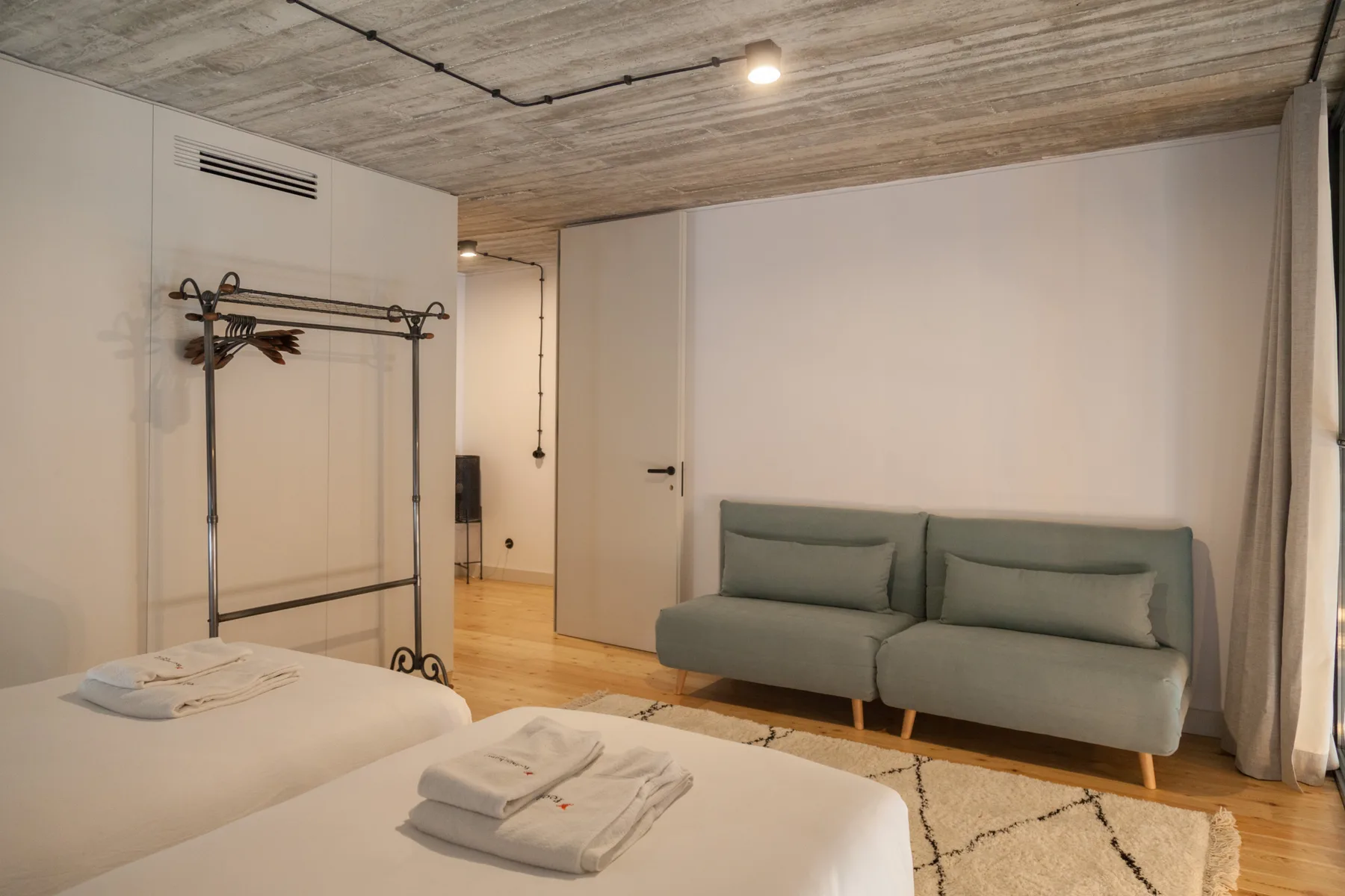 A bedroom with two beds, a clothing rack, and seating against the wall.