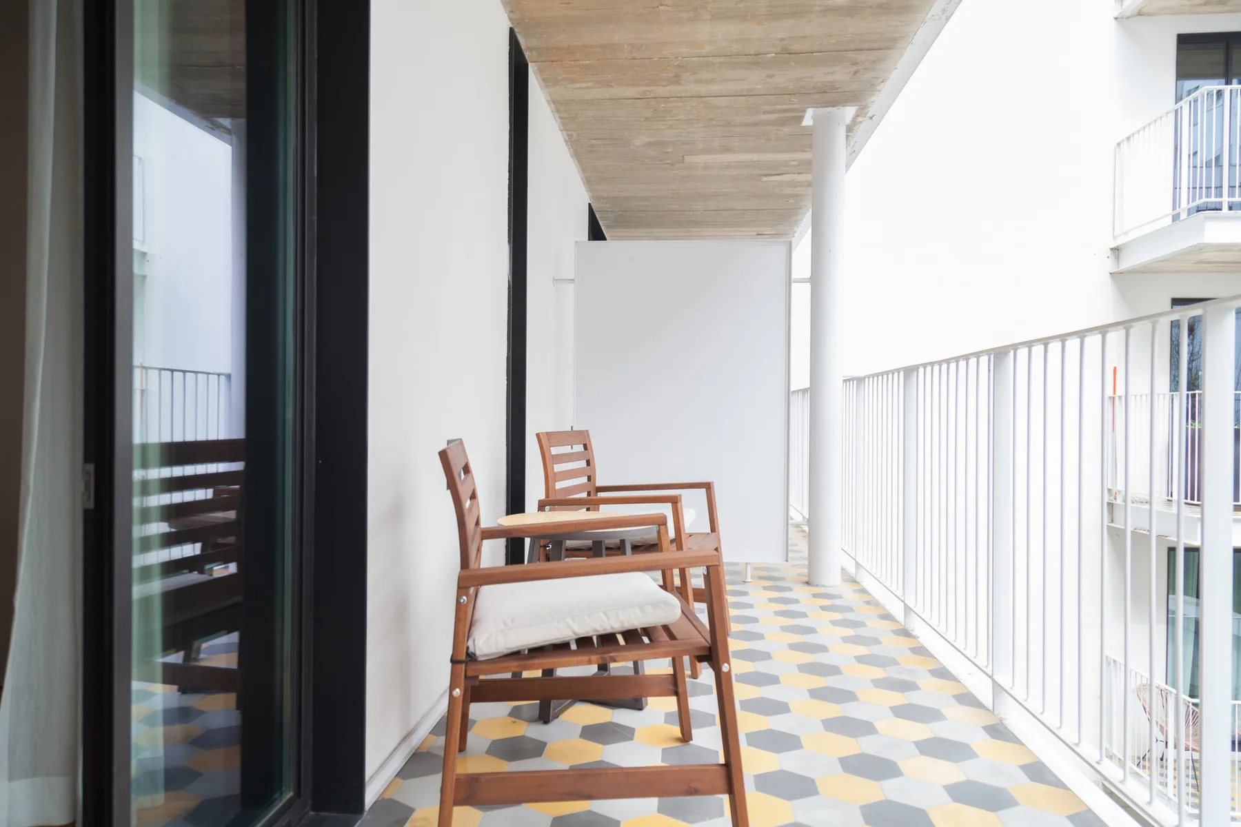 Una zona de estar en el balcón con sillas de madera junto a una puerta de cristal.