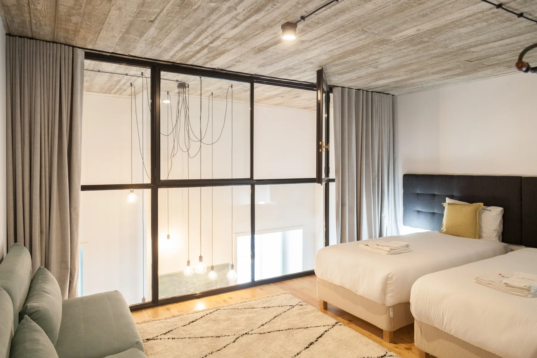 A bedroom with two beds, a seating area, and glass partitions.