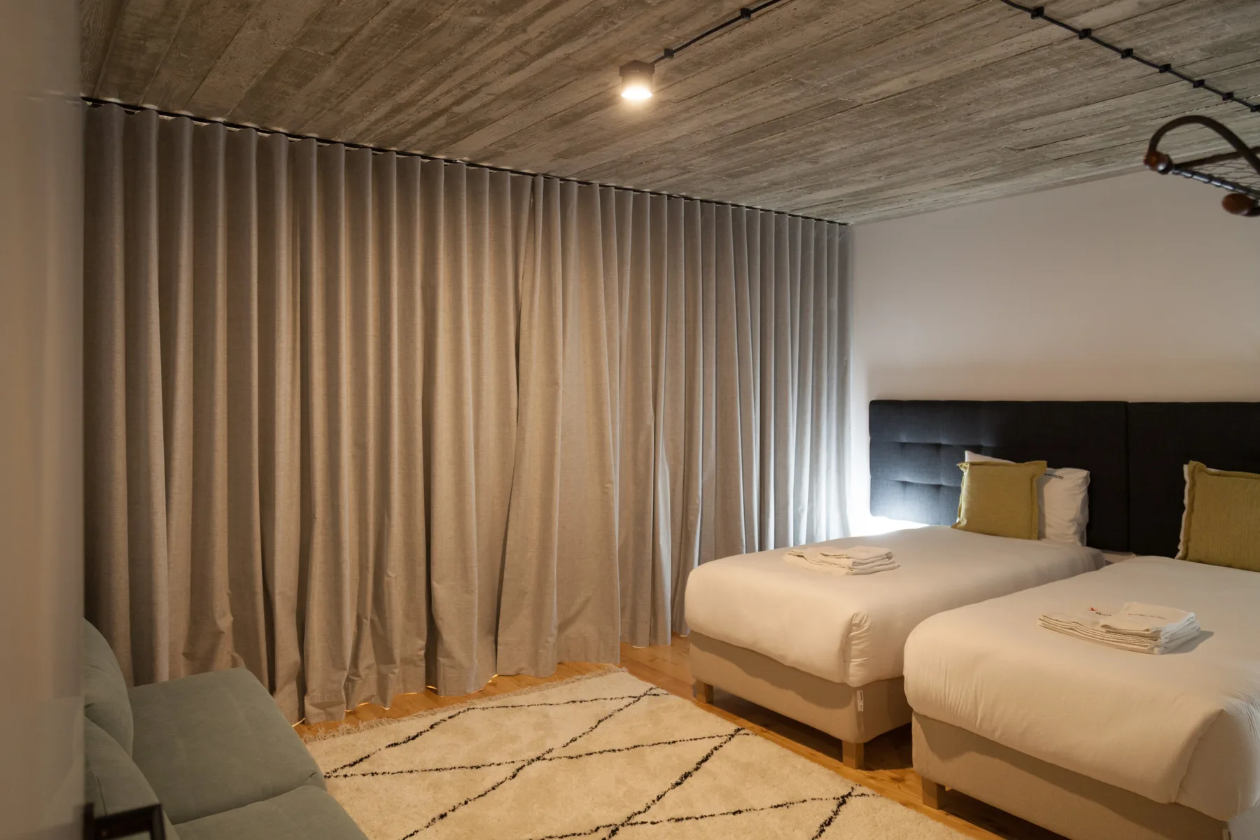 A bedroom with two beds, beige curtains, and a patterned rug.