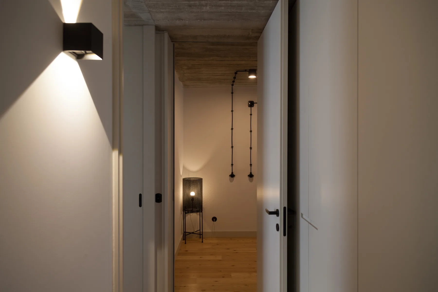 A hallway opens into a room with wood flooring and hanging lights.