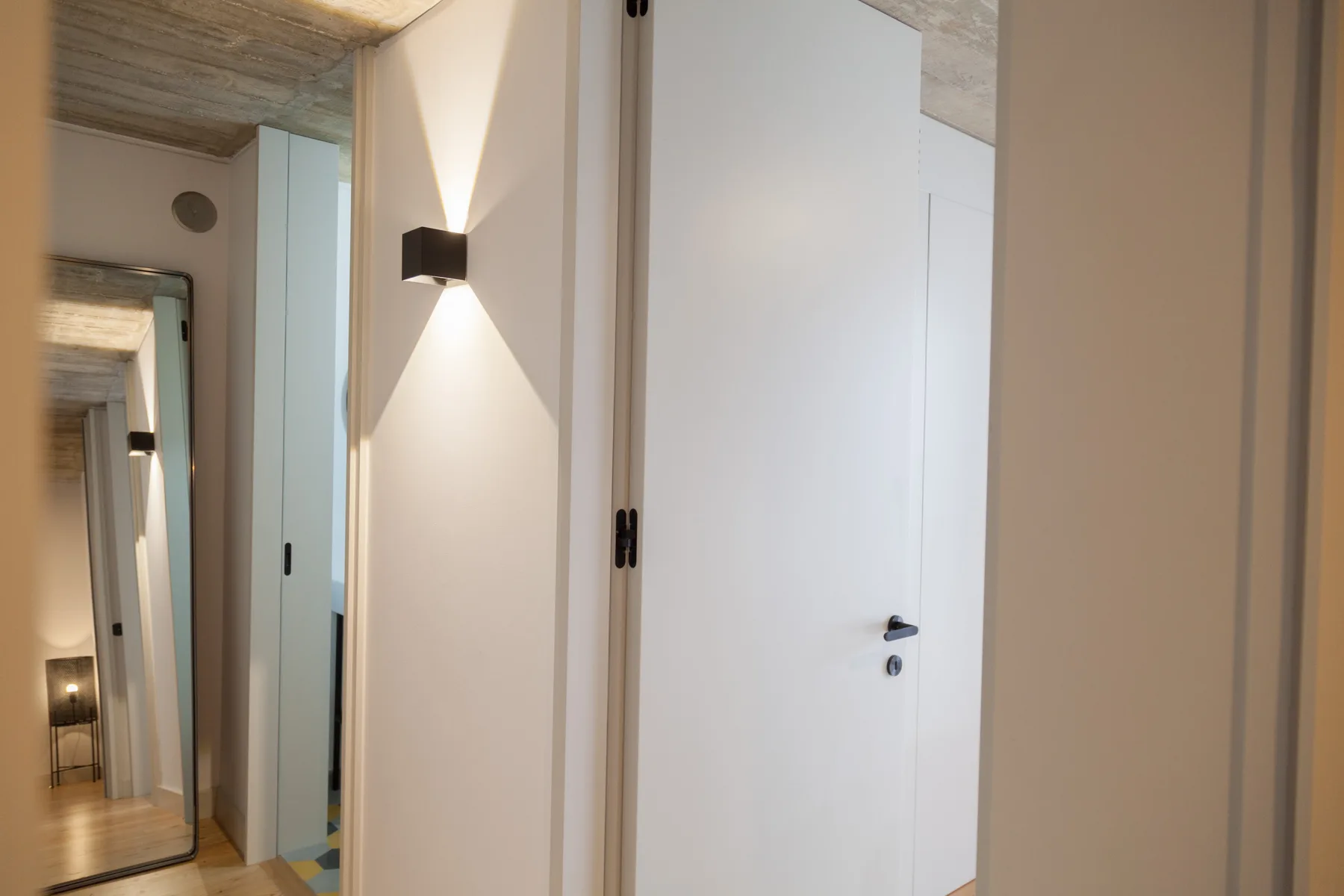 A bright interior hallway with white doors and a wall light.