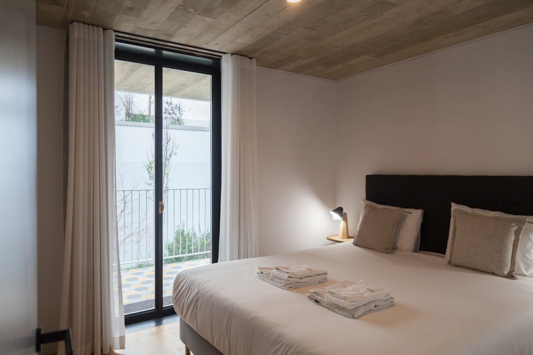 A bedroom with a neatly made bed beside a tall glass balcony door.