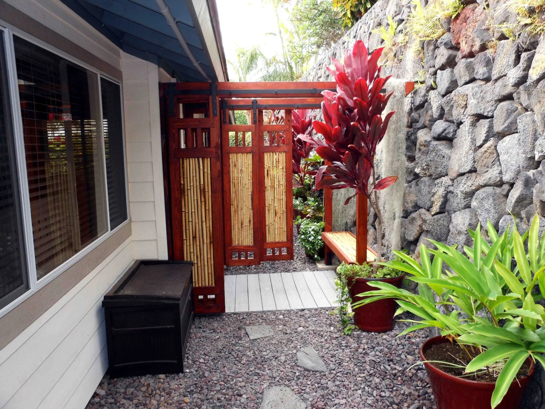 Un sendero de jardín exterior con una puerta de madera roja y plantas frondosas.
