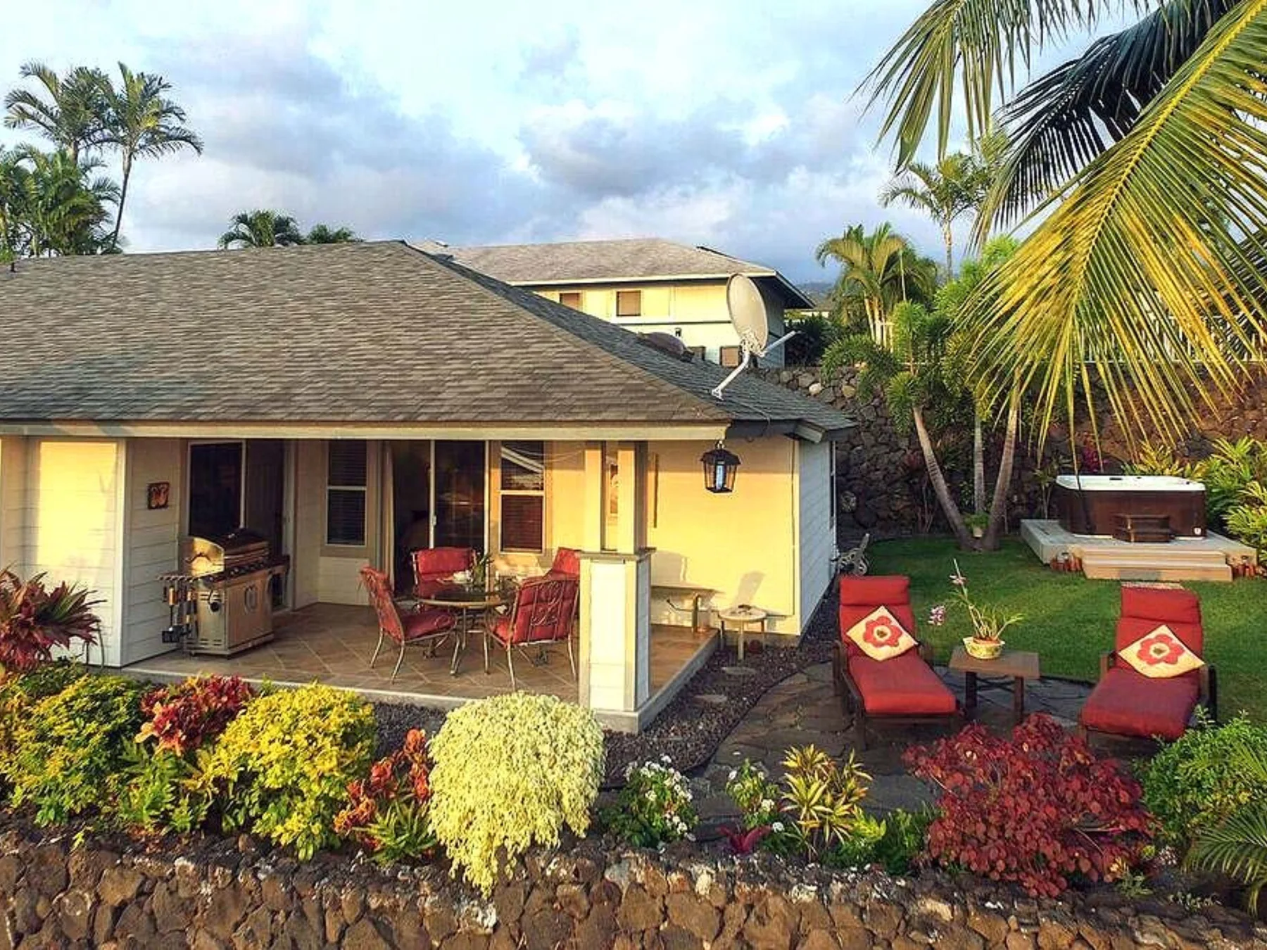 Una casa da a un patio con asientos al aire libre, plantas tropicales y una bañera de hidromasaje.