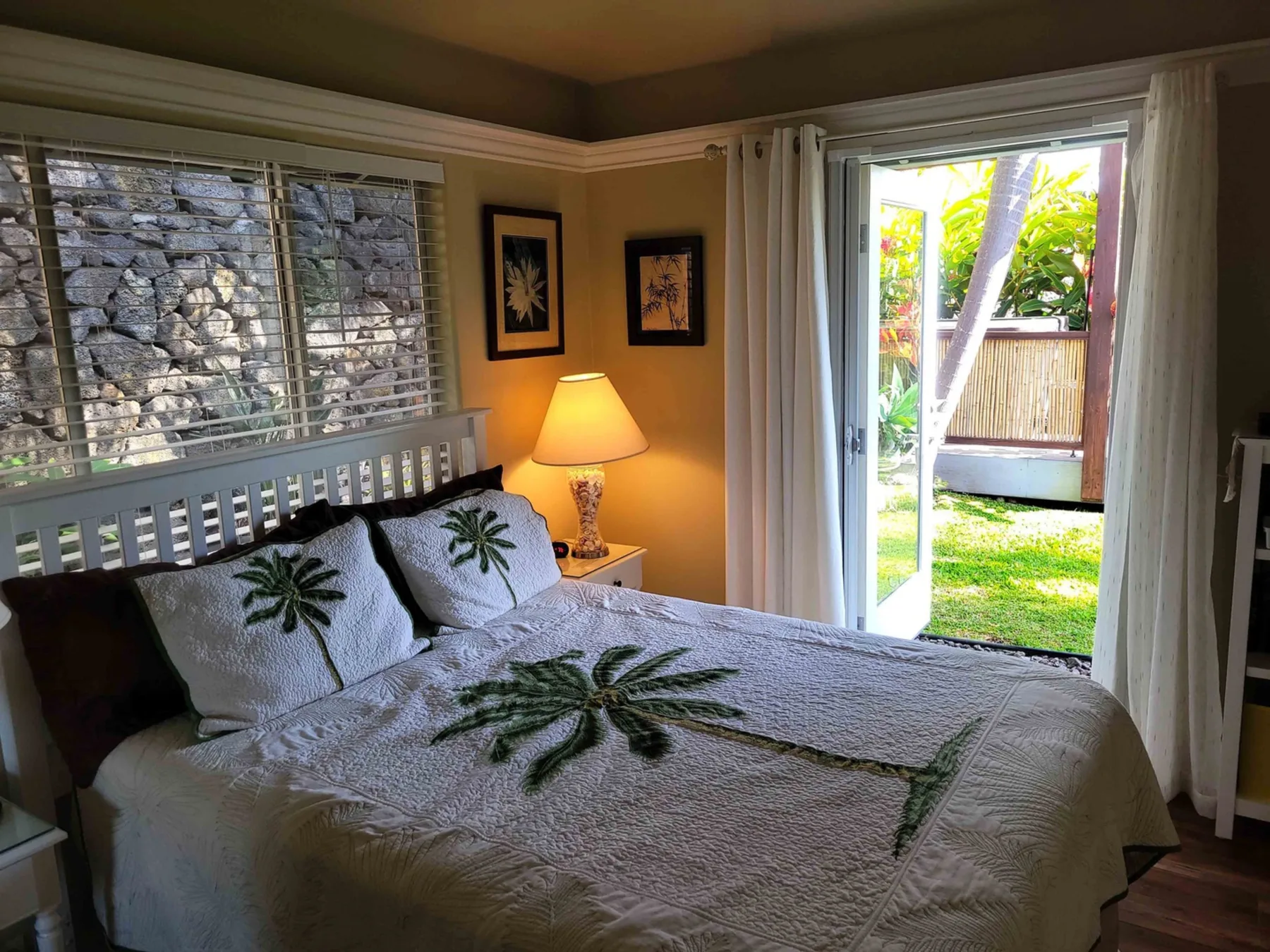 Un dormitorio con una cama tendida, una lámpara de noche y puertas abiertas al jardín.