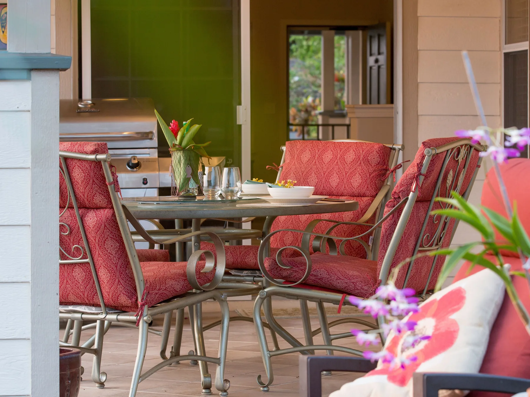 Un comedor en un patio cubierto con una mesa y asientos con cojines rojos.