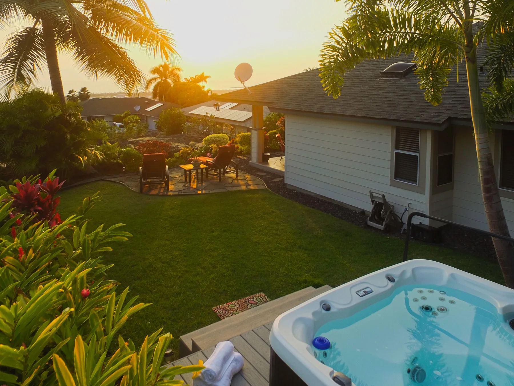 Un patio ajardinado con asientos al aire libre y una bañera de hidromasaje al atardecer.