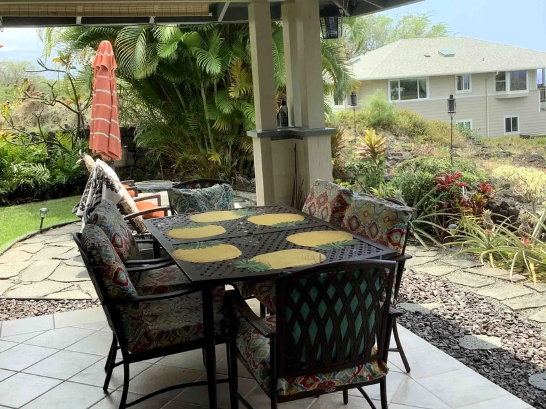 Un comedor exterior cubierto con una mesa y asientos acolchados entre plantas.