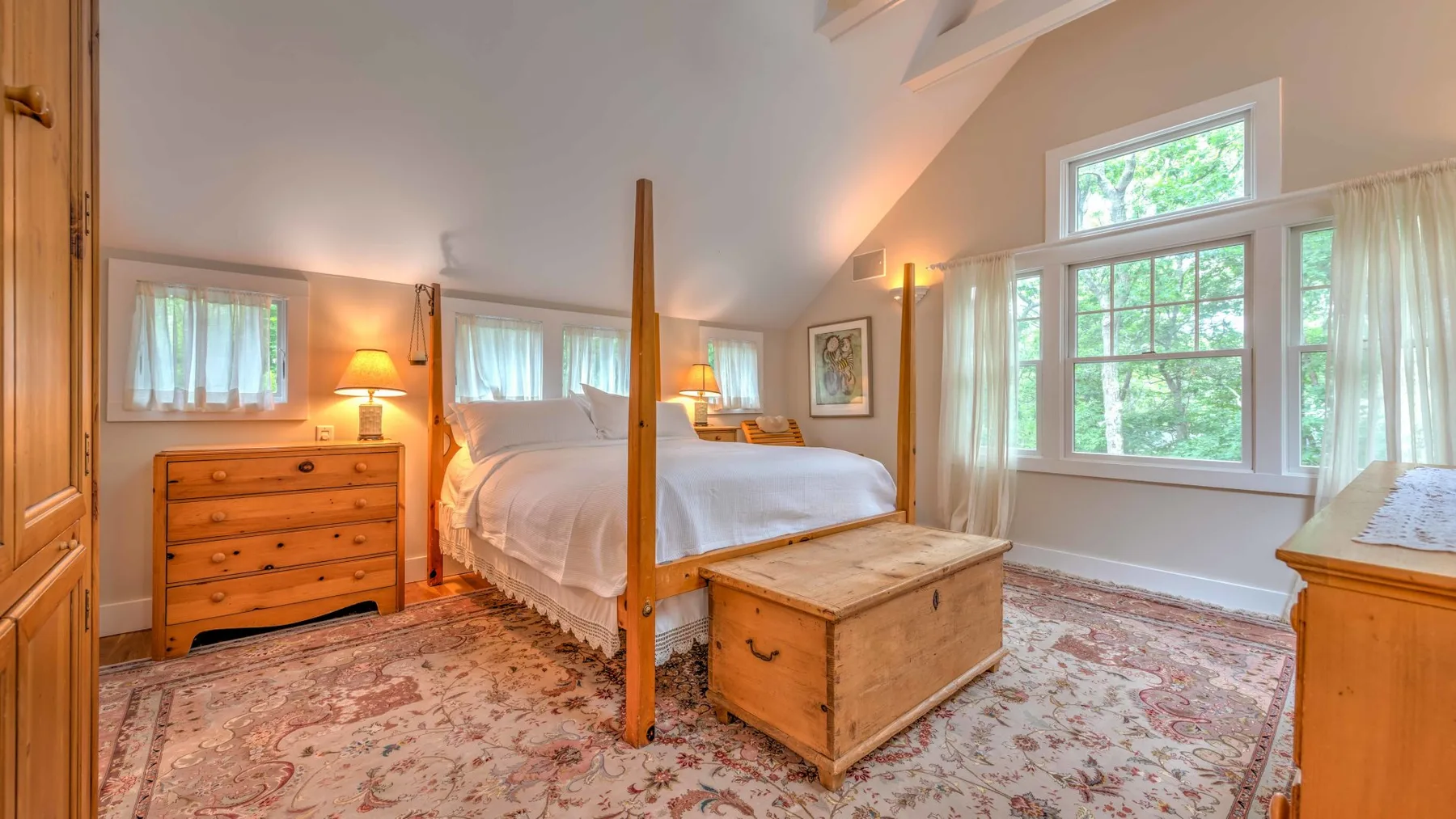A bright bedroom with a canopy bed, wooden chest, and large windows.