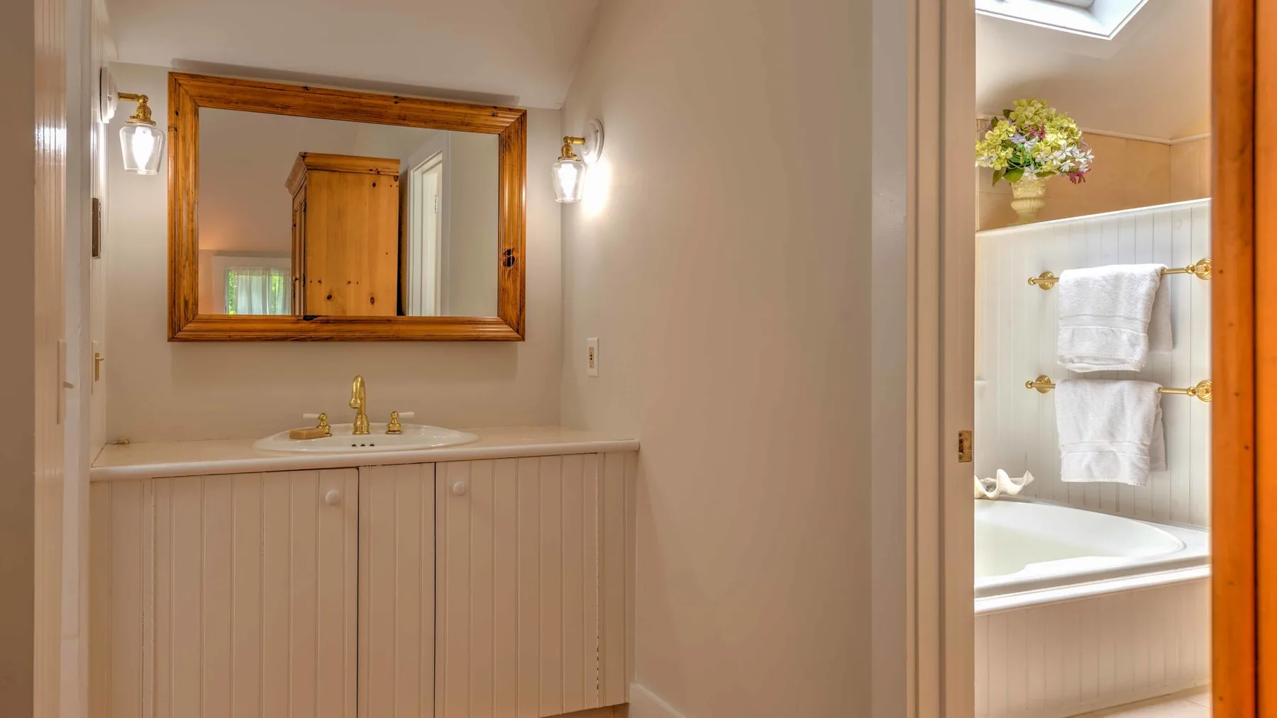 A bathroom vanity with a mirror sits beside a bathtub with towels.