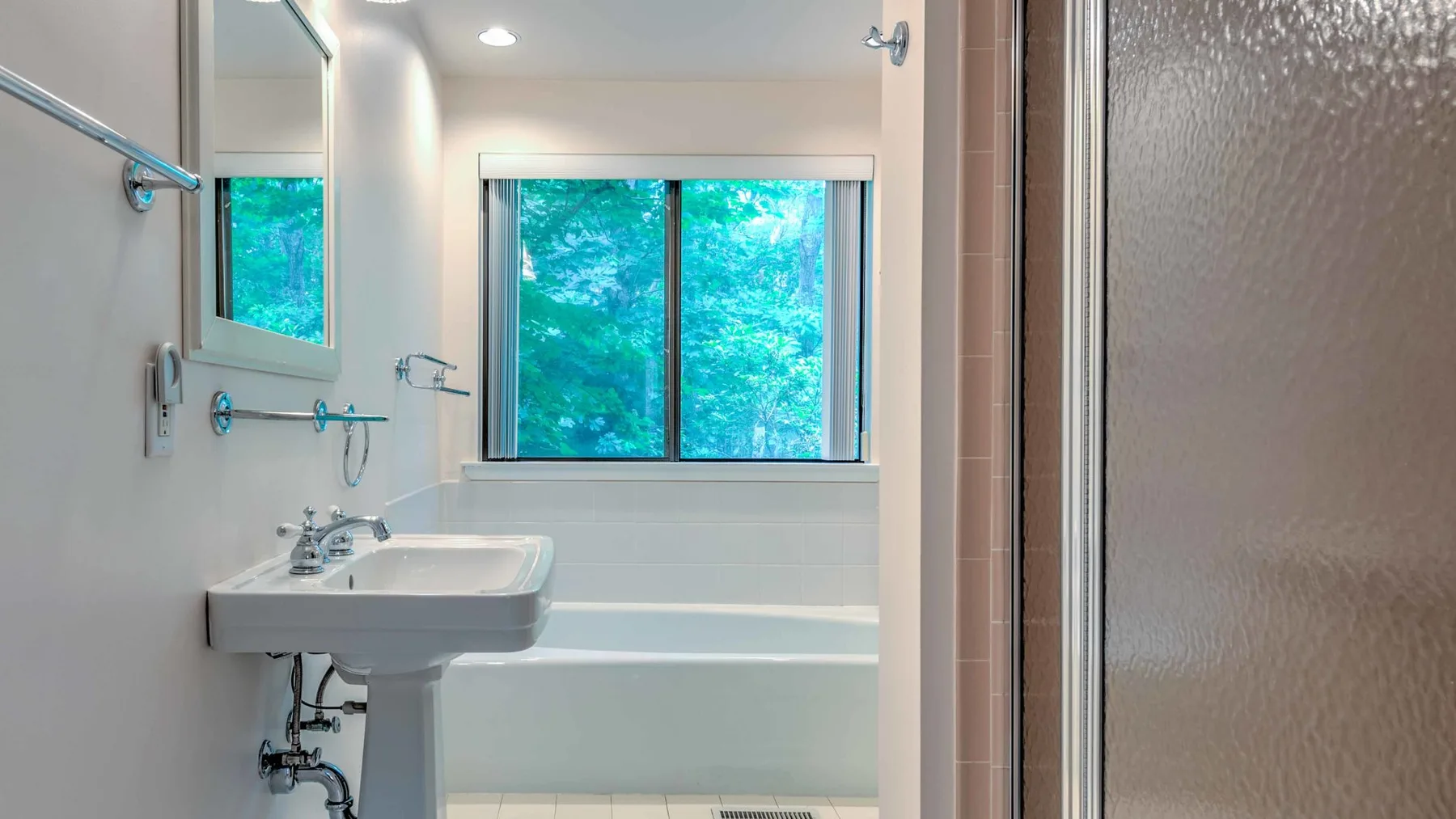 A bathroom with a sink, bathtub, and window overlooking greenery.