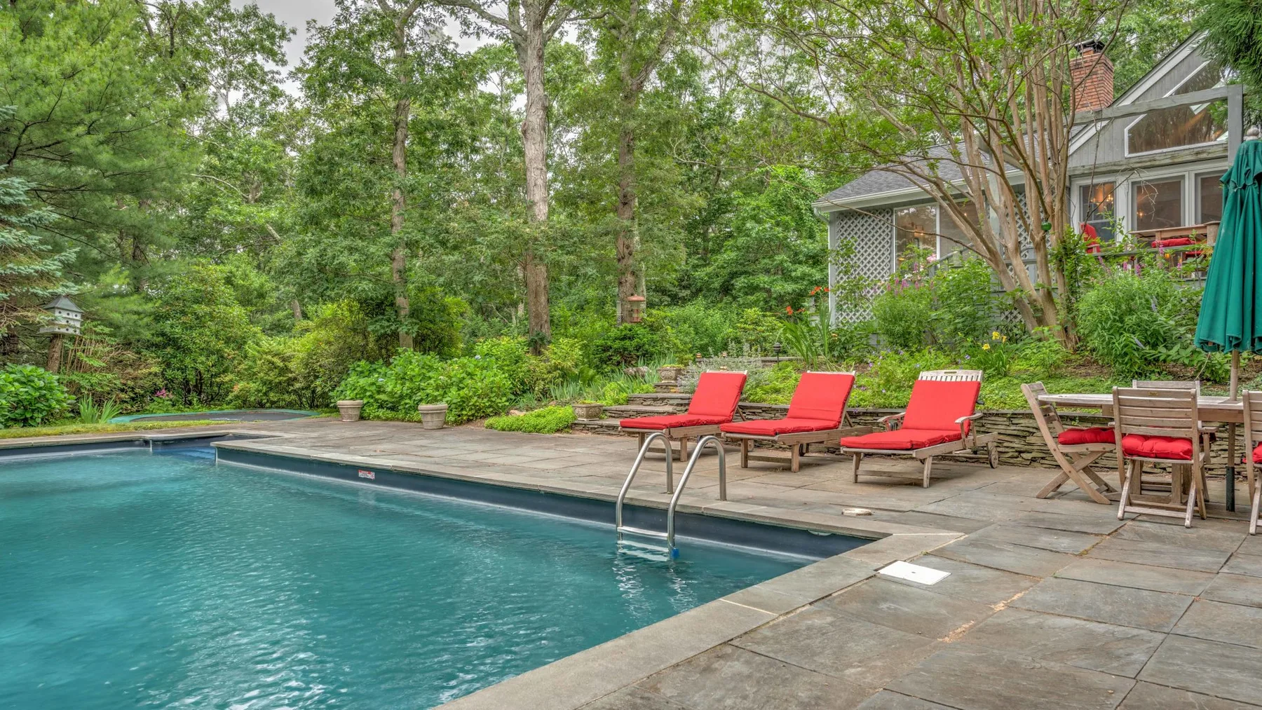 An outdoor swimming pool beside a paved patio with lounge seating and greenery.