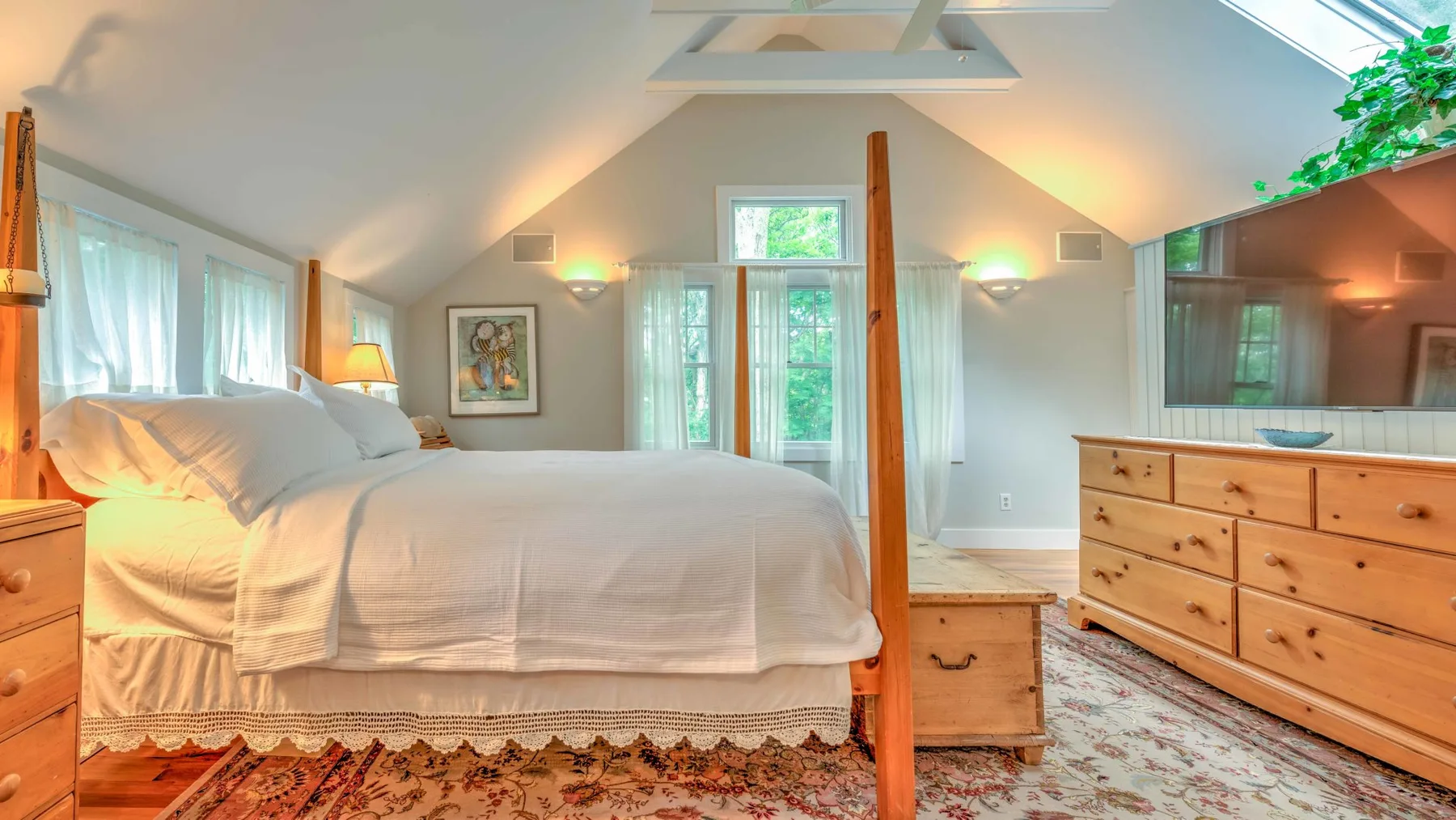 A bright bedroom with a large bed, wooden furnishings, and sloped ceilings.