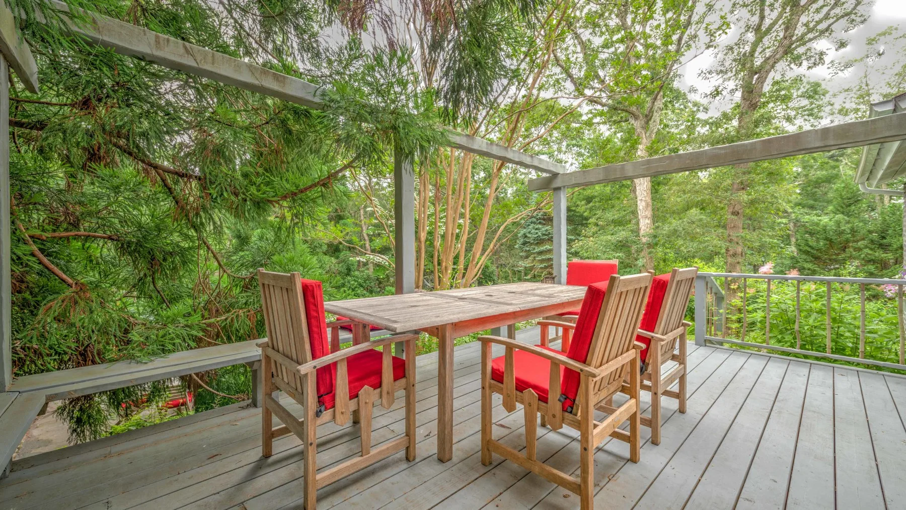 An outdoor deck with a wooden dining table and red-cushioned seating.