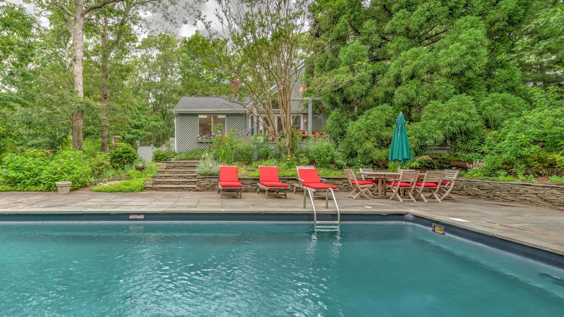 An outdoor swimming pool with red seating and trees surrounding the patio.