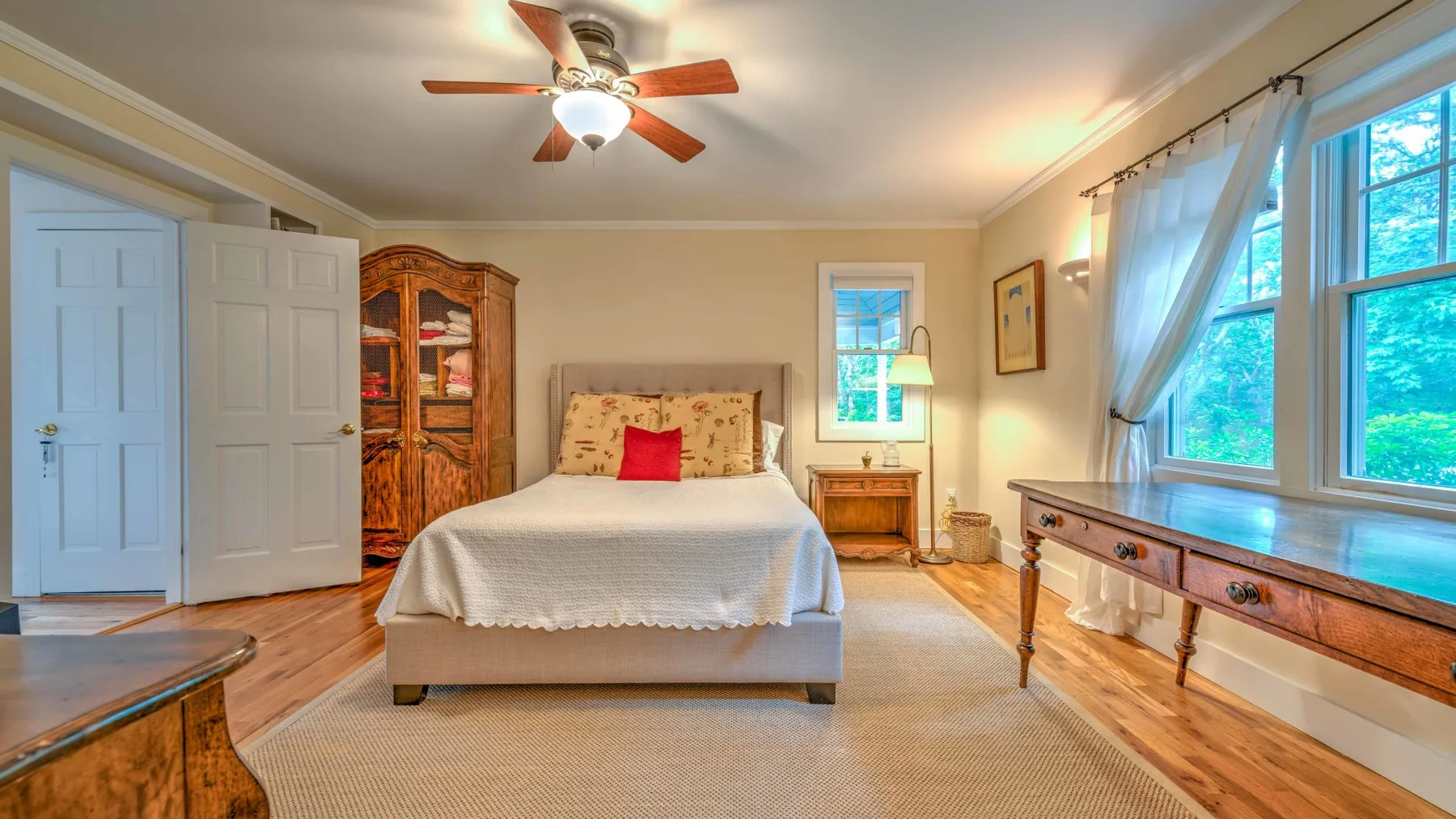 A bedroom with a bed, wooden cabinet, and large windows.