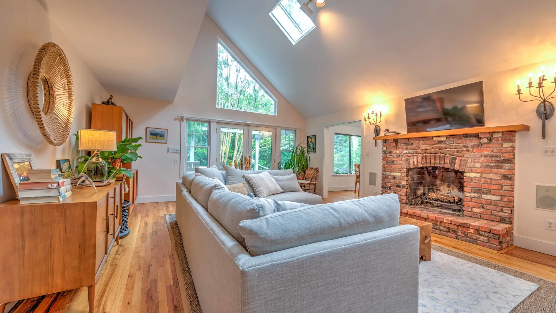 A bright living room with seating facing a brick fireplace and large windows.