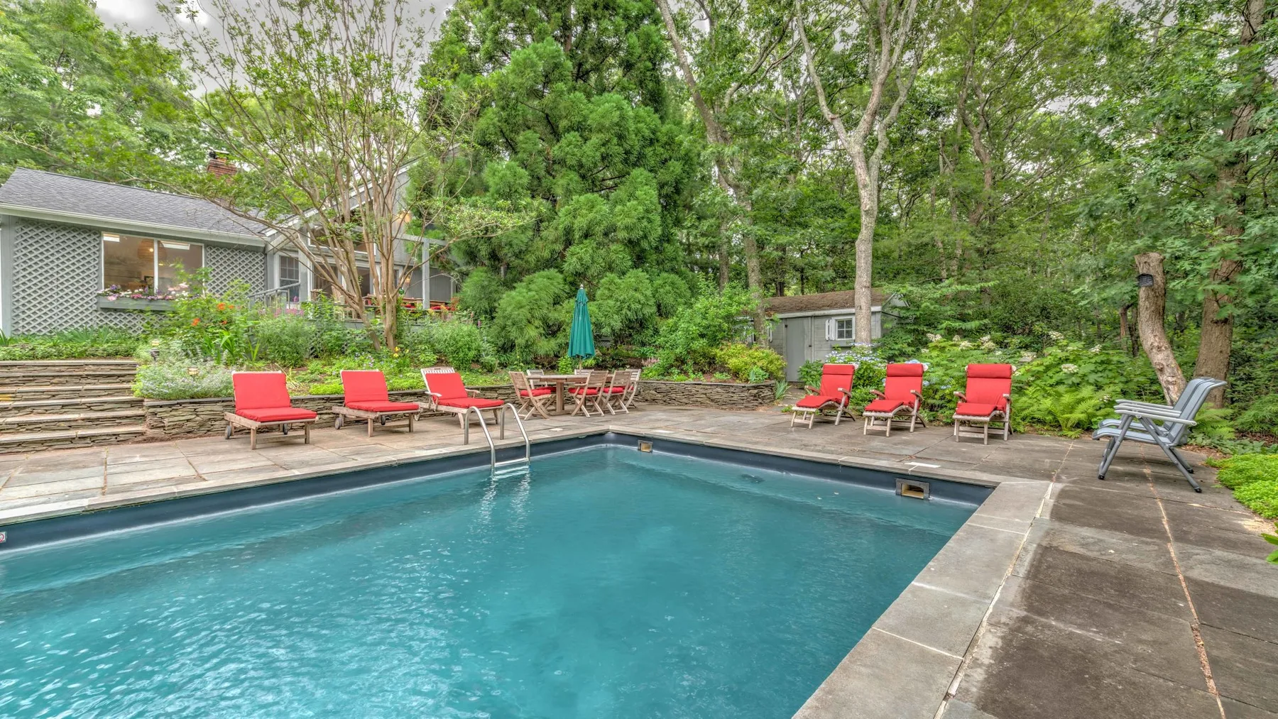 An outdoor swimming pool is surrounded by seating and leafy trees.