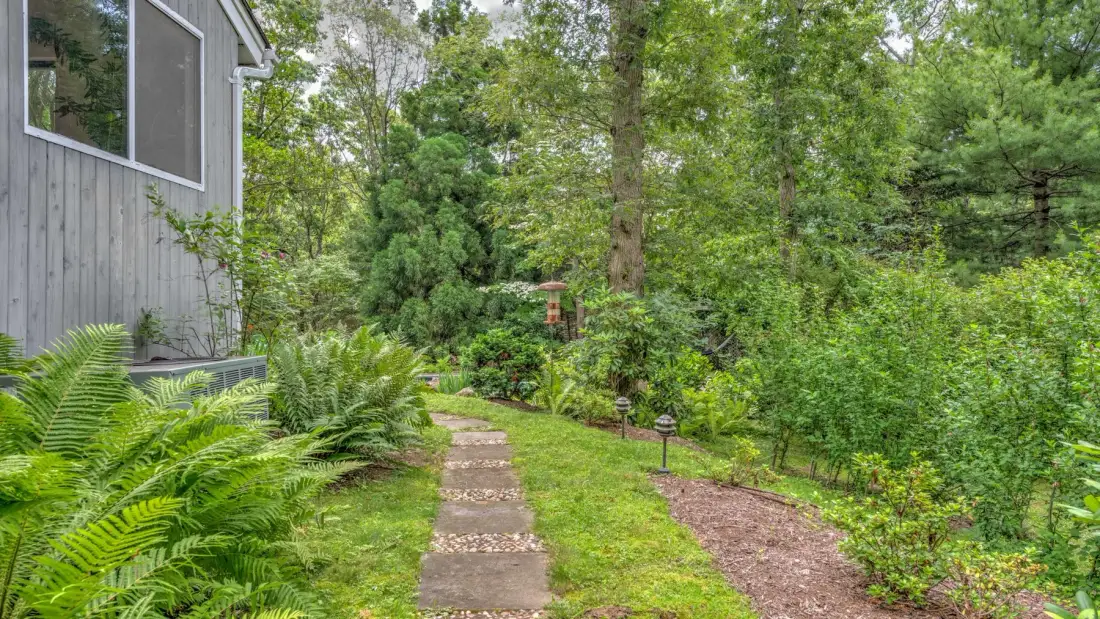 A garden path winds through green planting beside a wood-sided building.