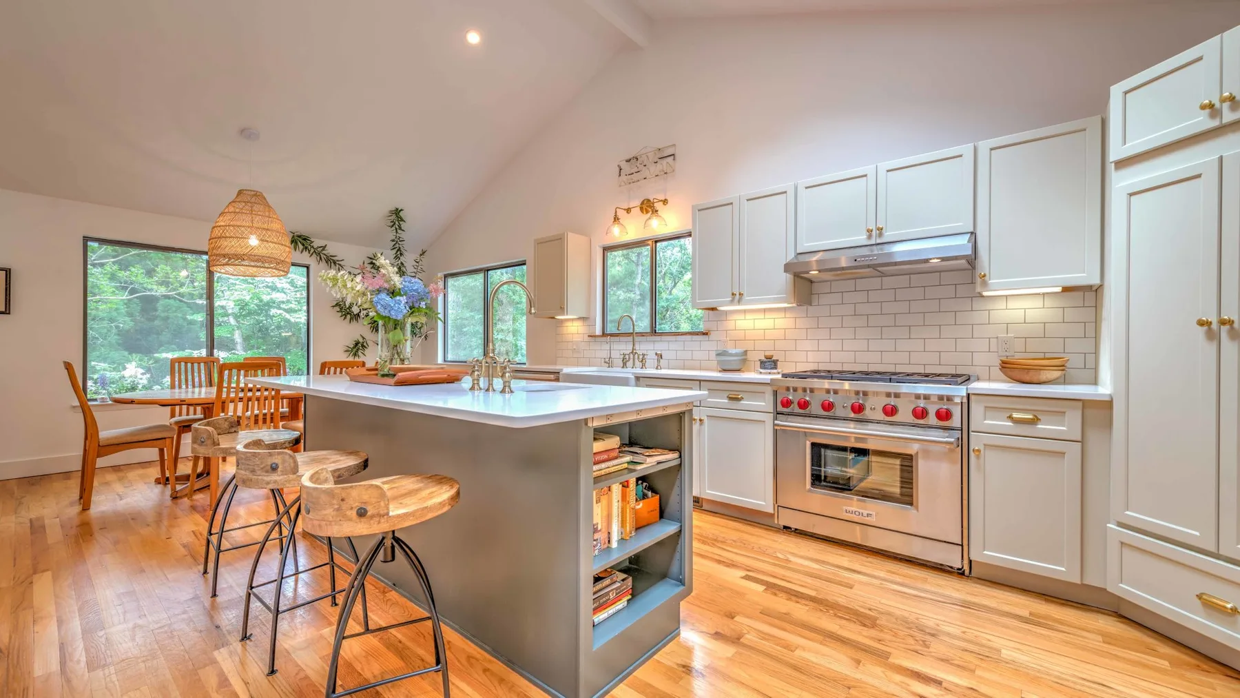A bright kitchen with a large island, wooden stools, and dining area.