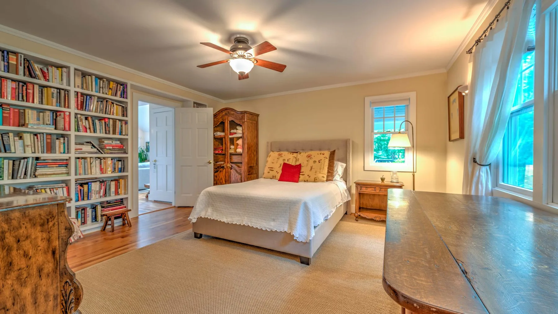 A bedroom with a bed, bookshelves, and large windows.