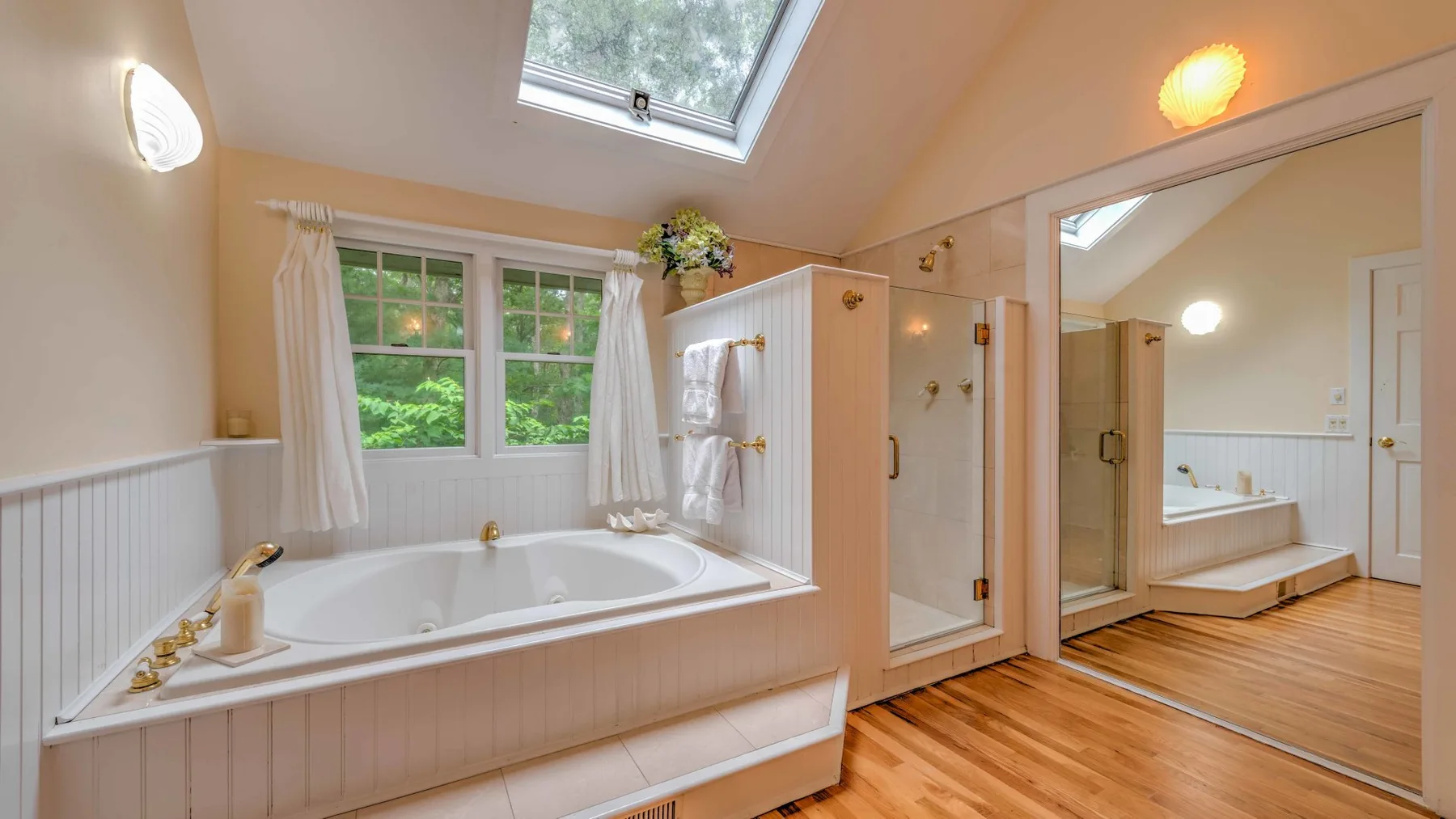 A bright bathroom with a built-in bathtub, glass shower, and skylight.
