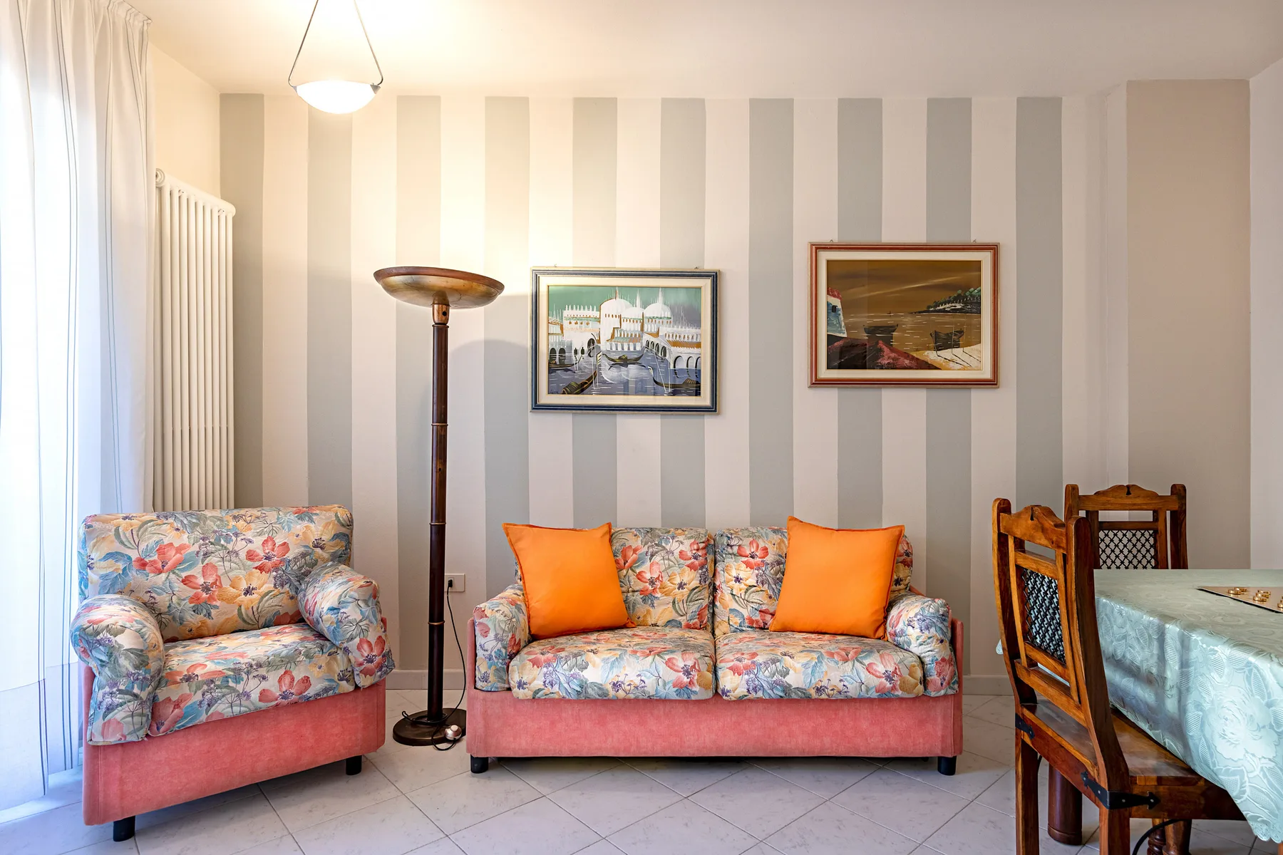 A living room with floral seating, orange cushions, and framed artwork on striped walls.