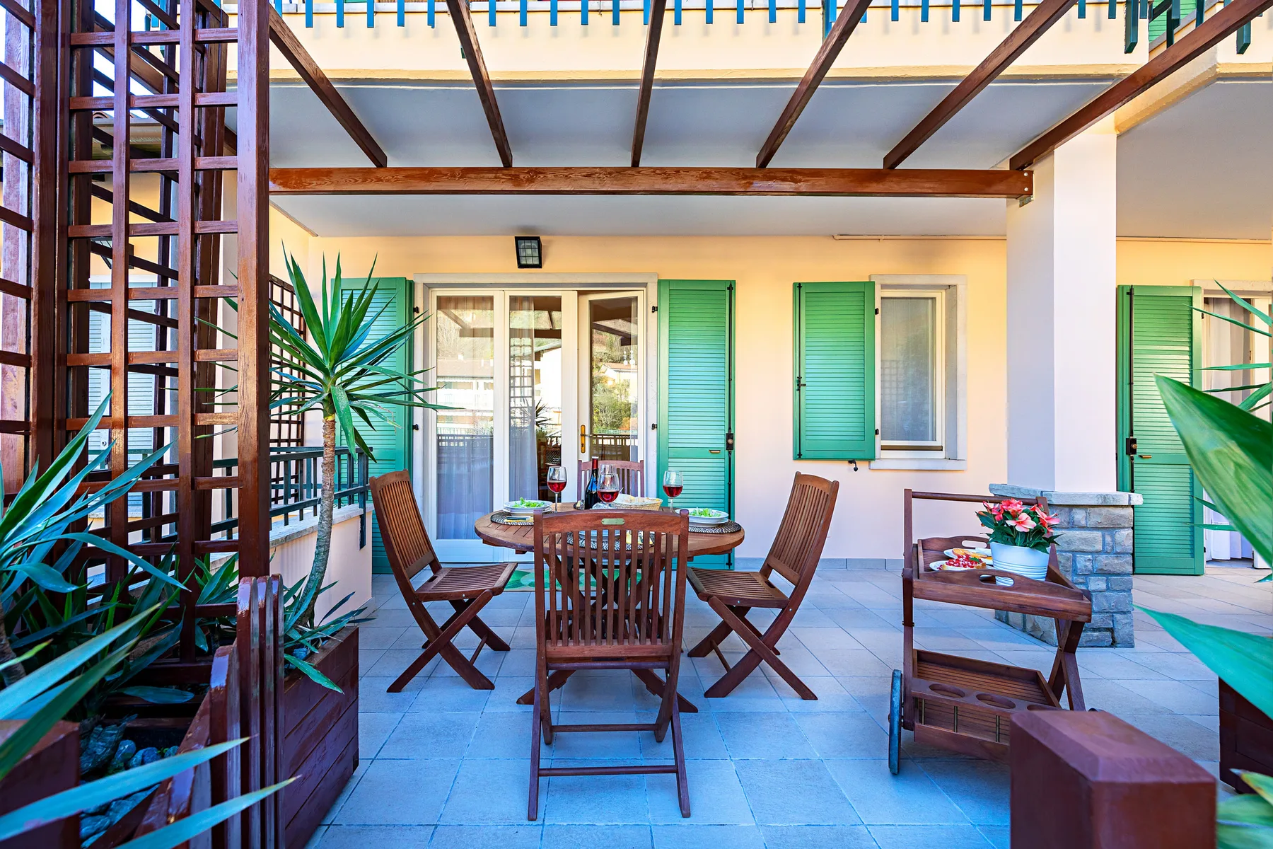 A covered outdoor dining area with wooden seating and green shutters.