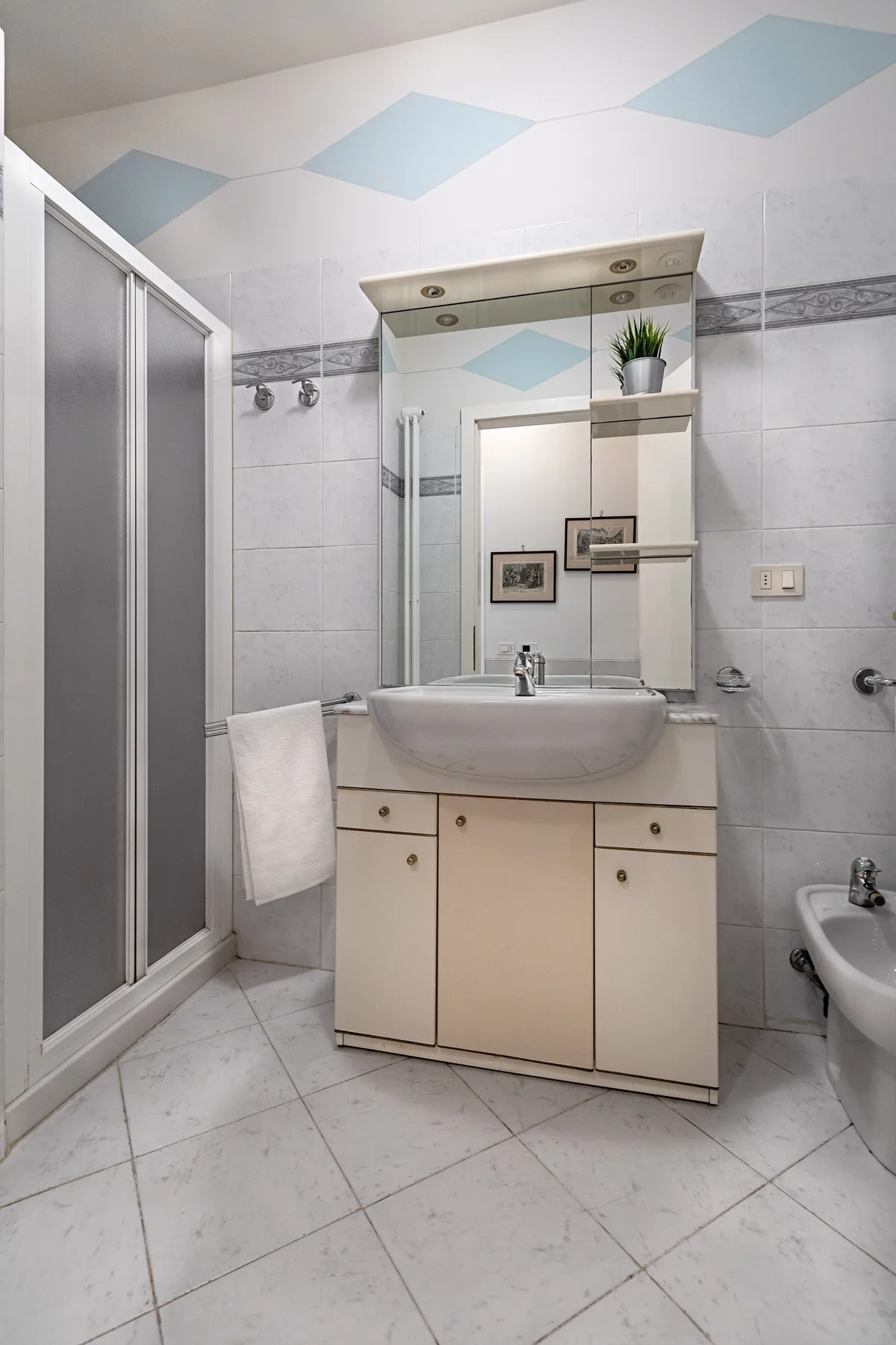 A tiled bathroom with a vanity, mirror, and glass shower enclosure.
