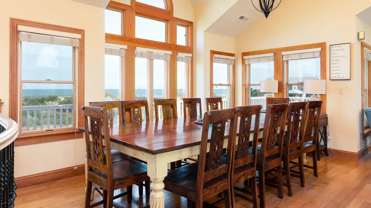 Un comedor con una mesa larga de madera y sillas junto a grandes ventanales.