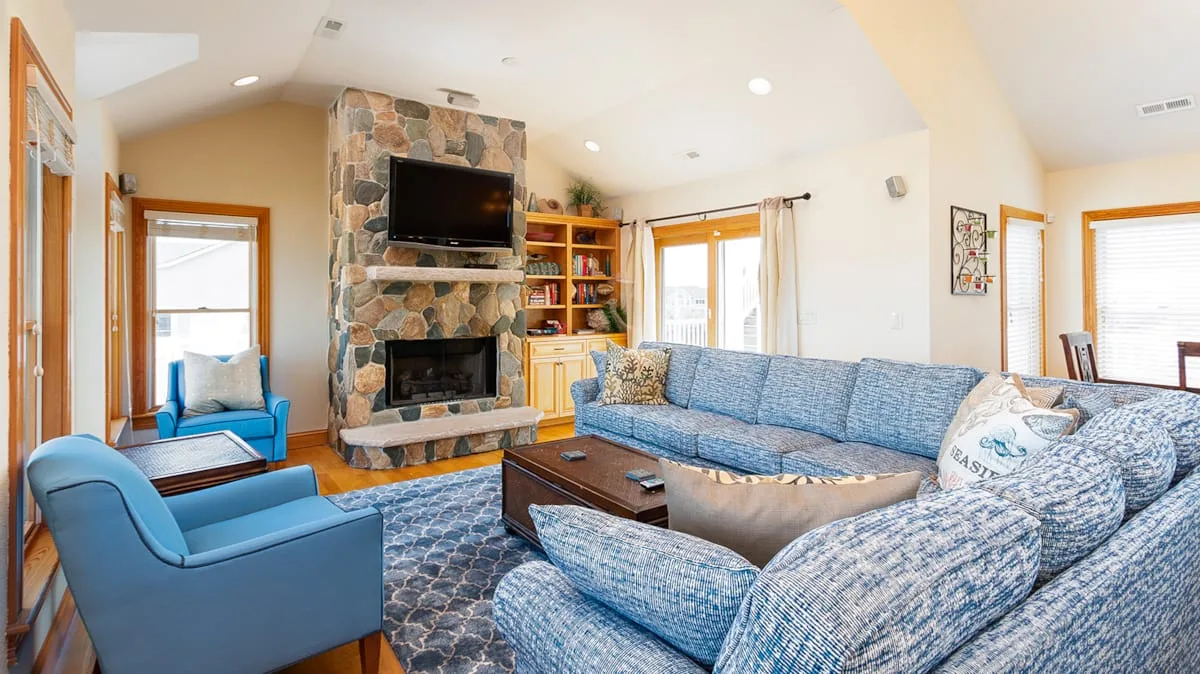 Una sala de estar con asientos azules junto a una chimenea de piedra y un televisor.