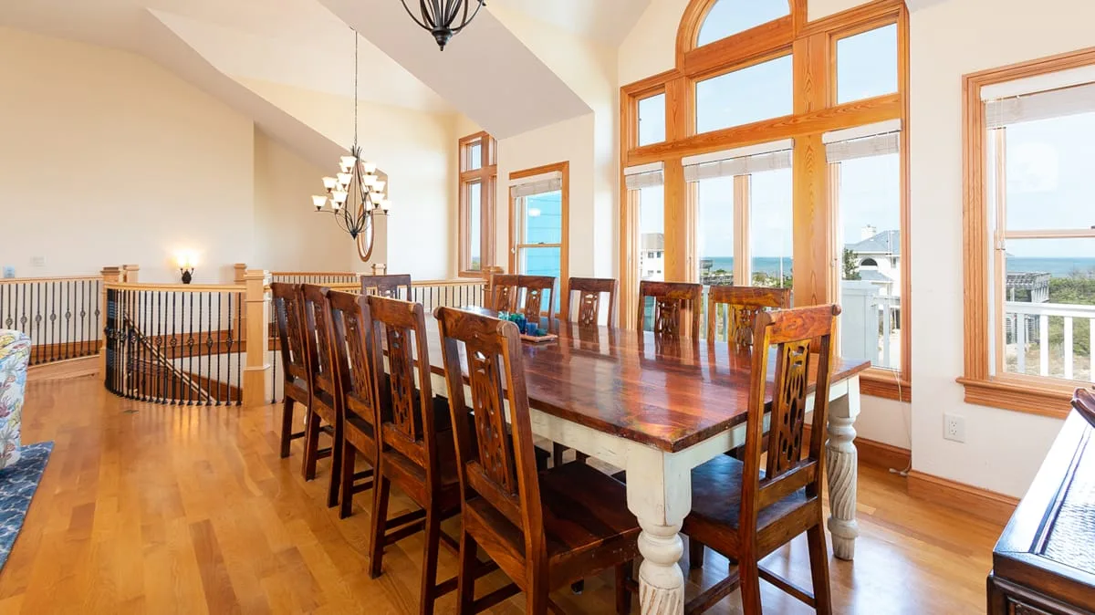 Un comedor con una mesa larga de madera y ventanas altas con vistas al agua.