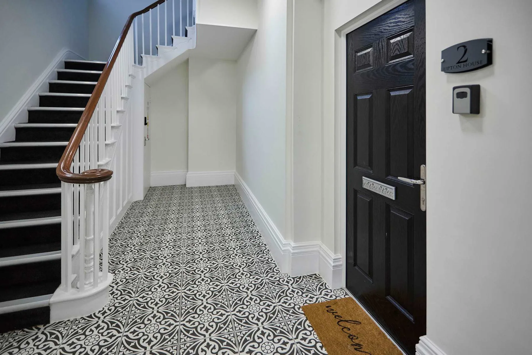 An entry hallway with patterned flooring, a staircase, and a dark door.