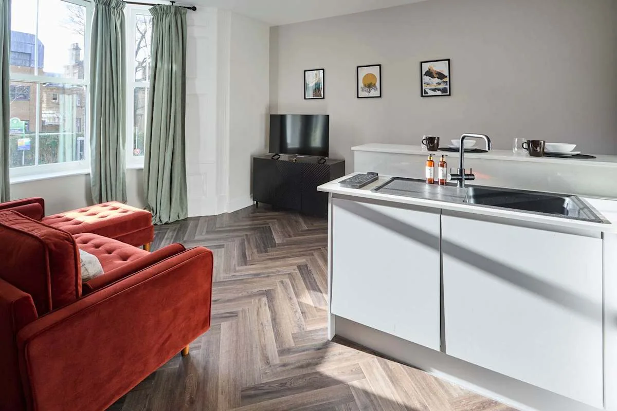 A living area with red seating sits beside a bright kitchen with a central island.