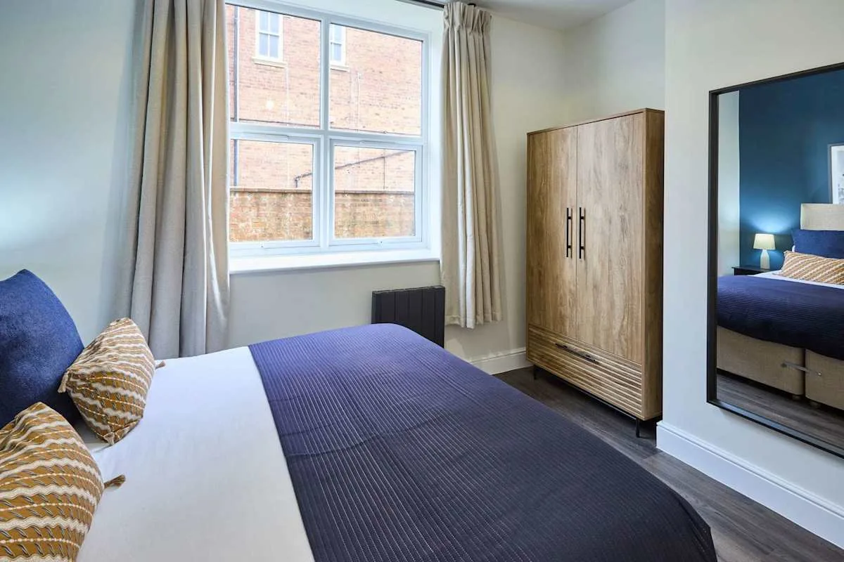 A bedroom with a bed beside a large window and a wooden wardrobe.