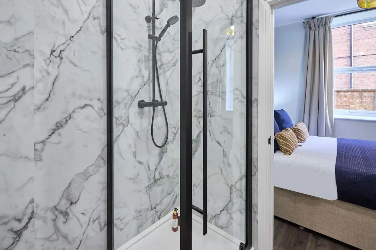 A marble-patterned shower opens onto a bedroom with a window.