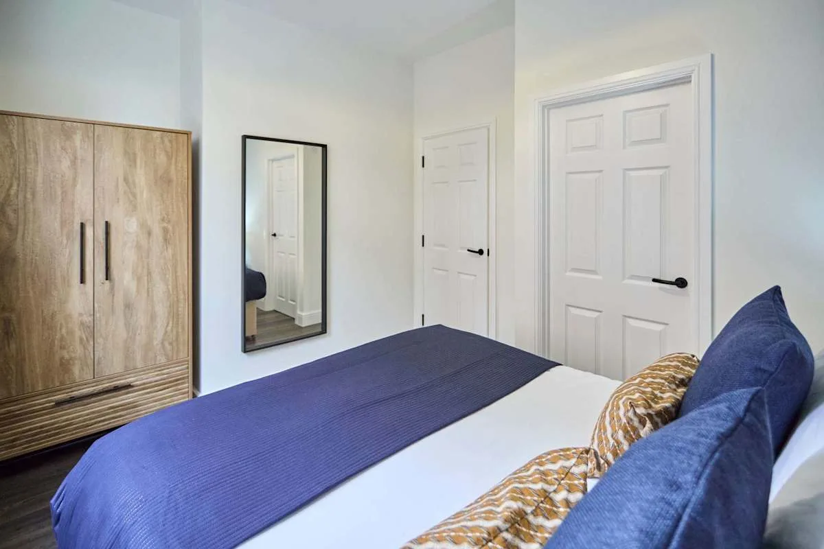 A bedroom with a bed dressed in blue and a wardrobe beside it.