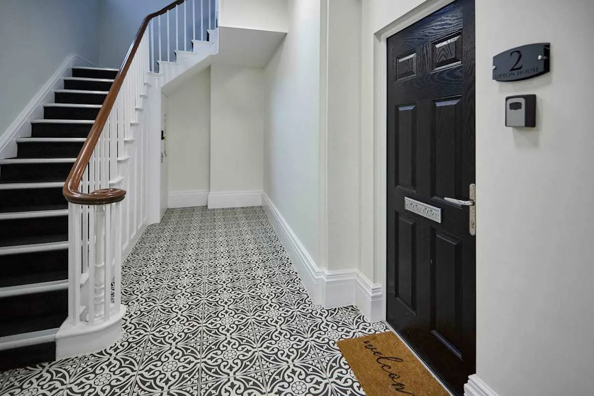 An entry hall with a staircase, patterned floor, and dark doorway.