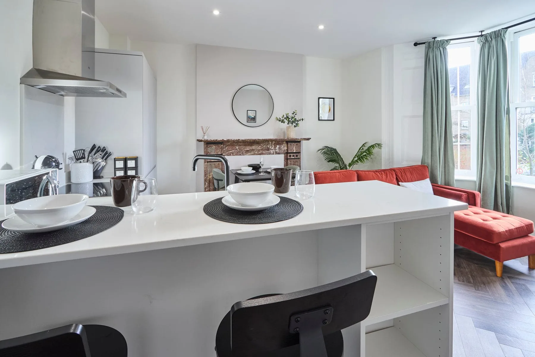 A bright open-plan kitchen and living area with a white breakfast bar and red seating.