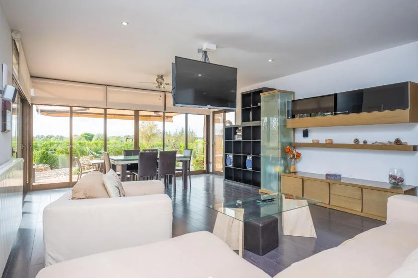 A bright living room opens onto a dining area and a garden through large windows.