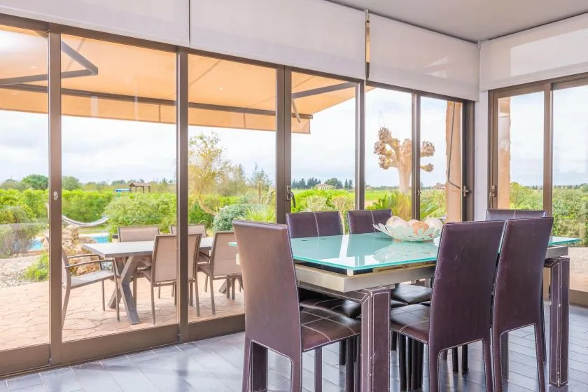 A dining area with a glass-topped table and large windows overlooking a garden.