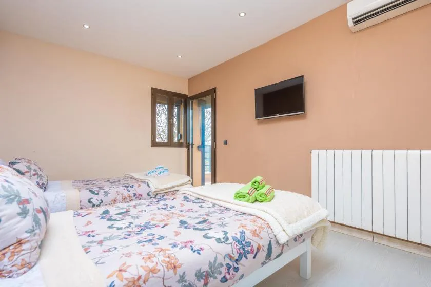 A bedroom with floral bedding, a wall-mounted television, and an air conditioner.