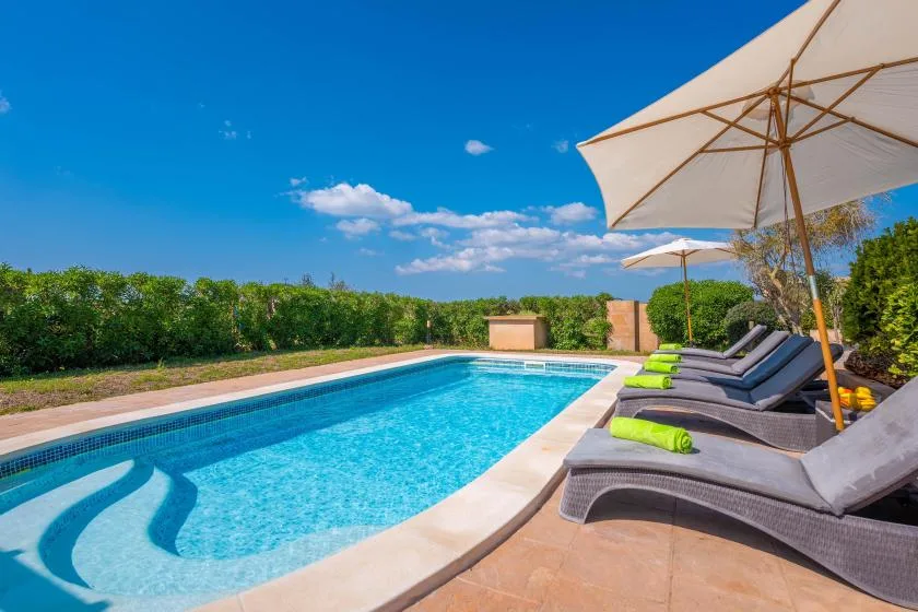 An outdoor swimming pool beside lounge seating and large sun umbrellas.