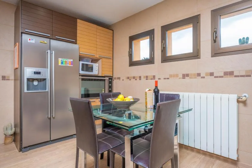 A kitchen and dining area with a glass table, seating, and stainless-steel appliances.
