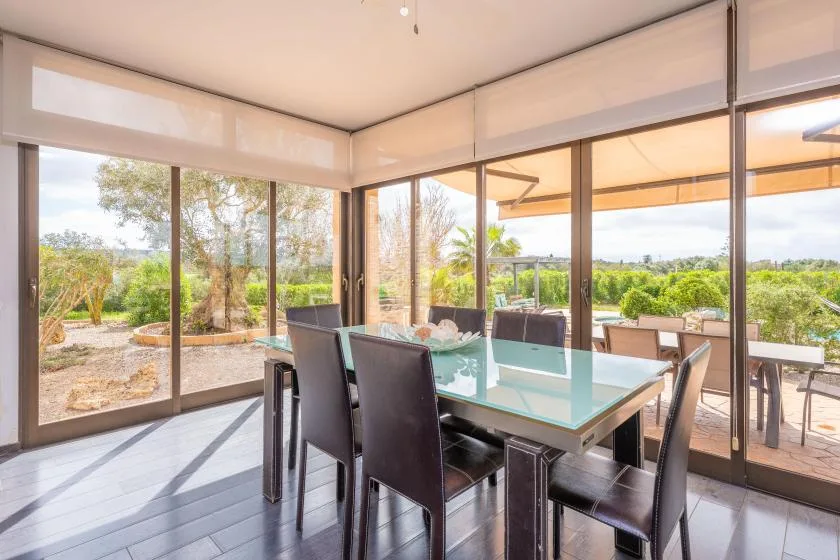 A dining area with a glass table and large windows overlooking a garden.
